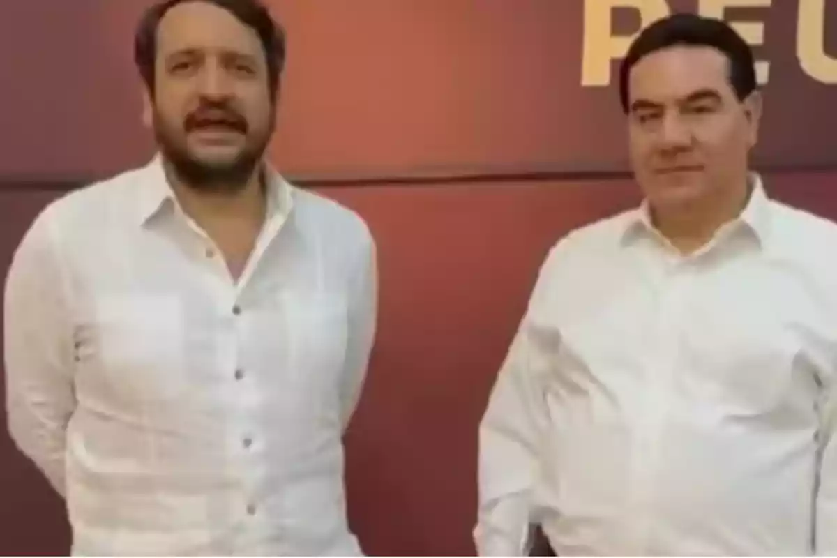 Dos hombres de pie con camisas blancas frente a un fondo marrón.