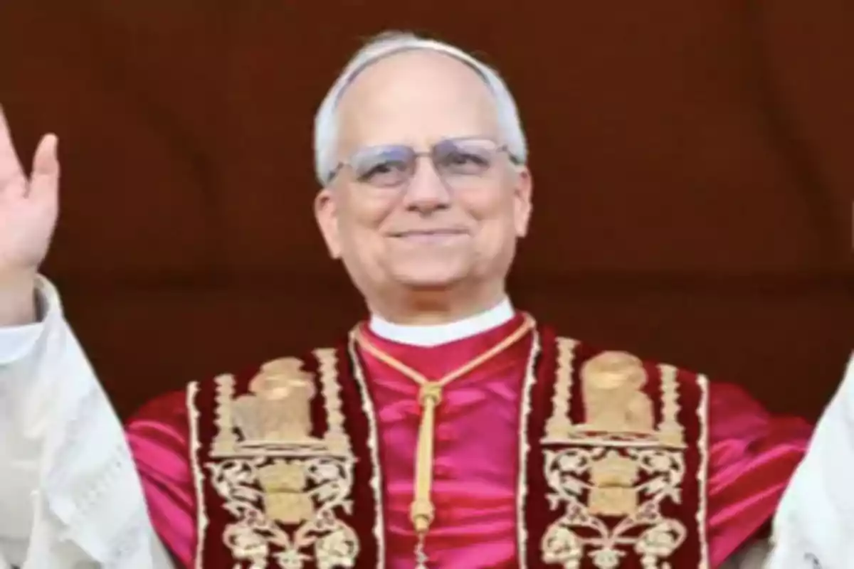 Un hombre mayor con gafas y vestimenta ceremonial religiosa sonríe y levanta las manos. Un hombre mayor con gafas y vestimenta ceremonial religiosa sonríe y levanta las manos.