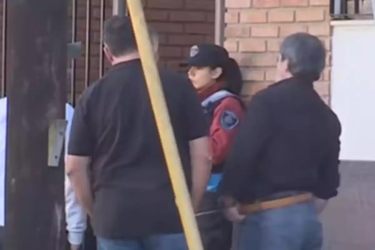 Un grupo de personas, incluyendo a una mujer con uniforme policial, se encuentra de pie frente a un edificio de ladrillos.