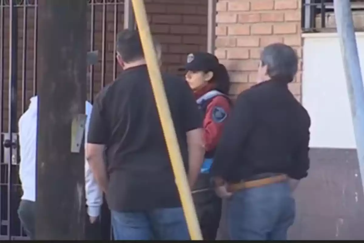 Un grupo de personas, incluyendo a una oficial de policía, está reunido frente a un edificio de ladrillos.