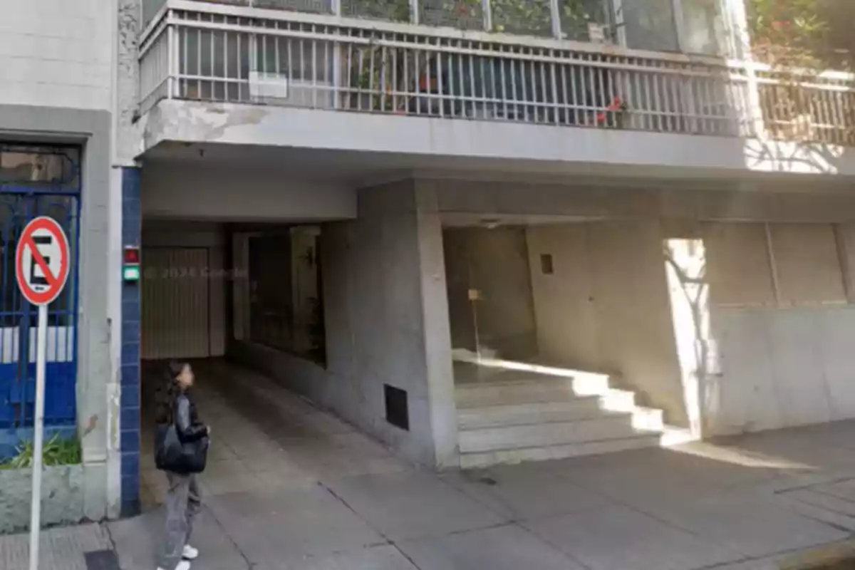Una persona está de pie en la acera frente a la entrada de un edificio con un letrero de no estacionar al lado.