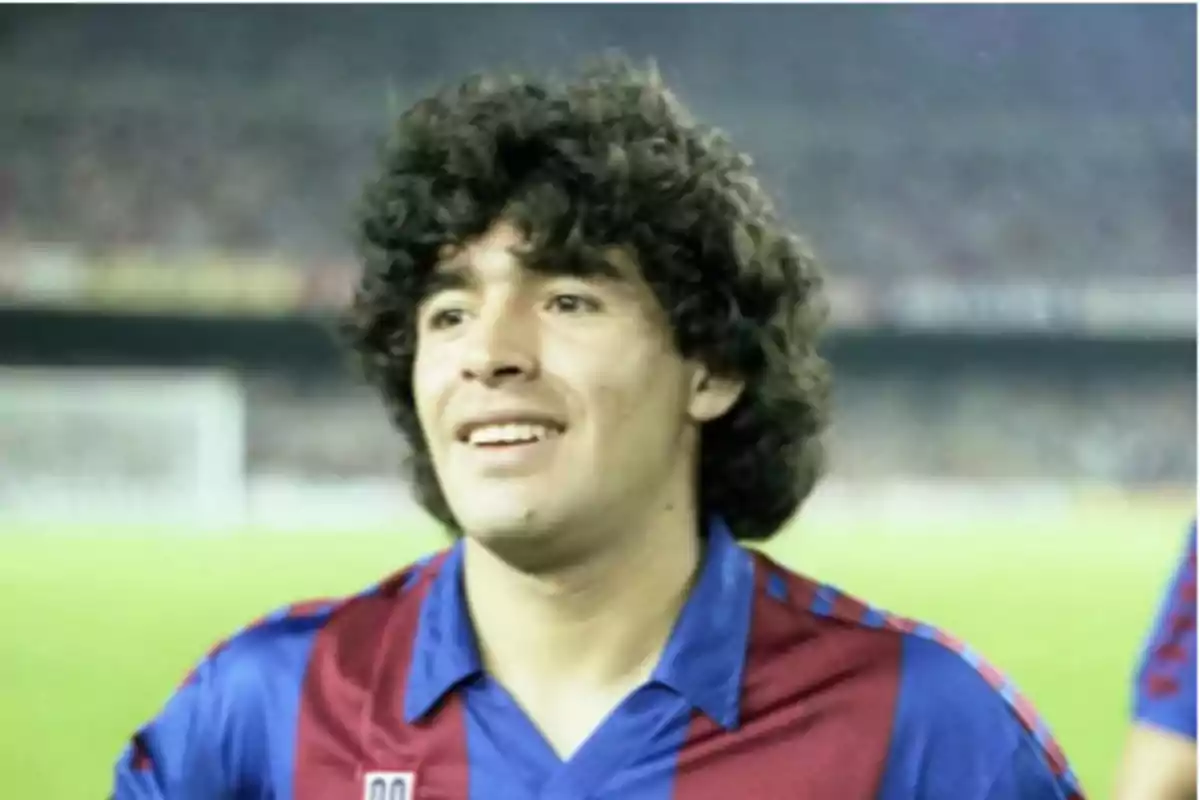 Un jugador de fútbol con cabello rizado lleva una camiseta azul y roja en un estadio.
