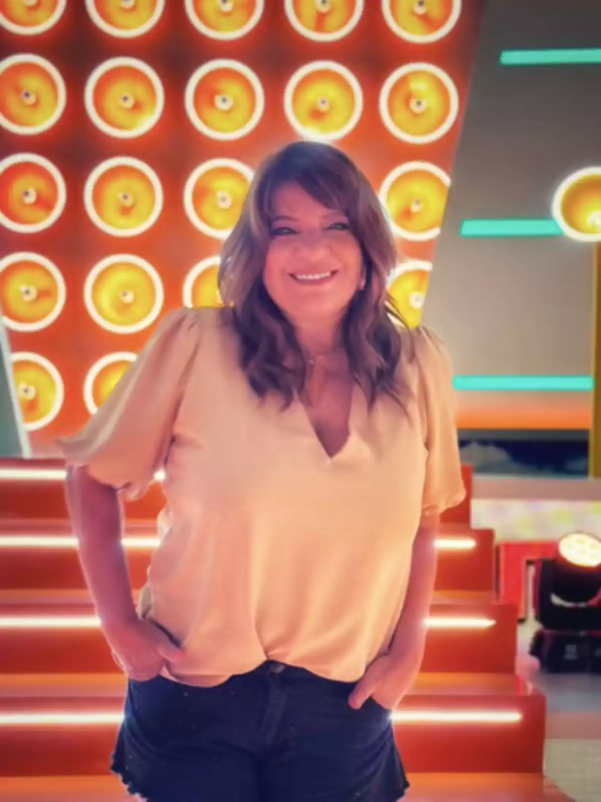 Mujer sonriendo de pie frente a un fondo colorido con luces circulares y escalones iluminados. Mujer sonriendo de pie frente a un fondo colorido con luces circulares y escalones iluminados.