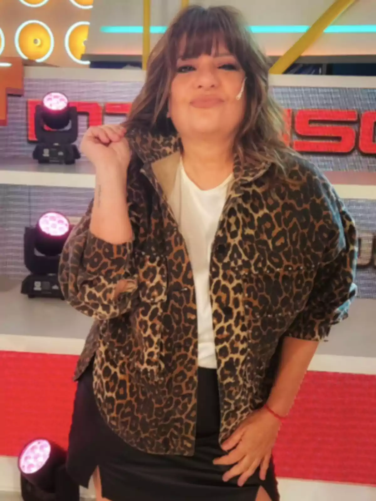 Una persona con chaqueta de estampado animal y falda negra posa frente a un fondo colorido en un estudio. Una persona con chaqueta de estampado animal y falda negra posa frente a un fondo colorido en un estudio.