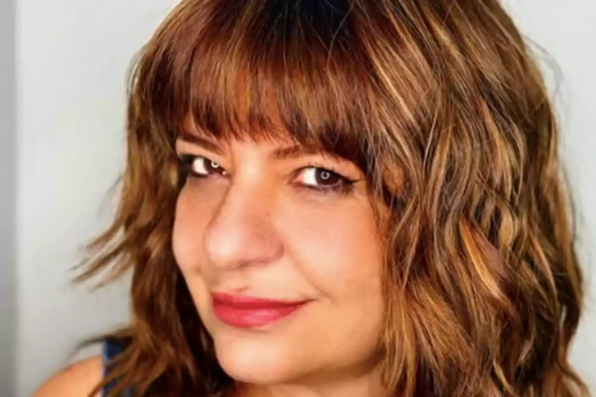Una persona con cabello castaño y ondulado mirando a la cámara con una expresión amigable.