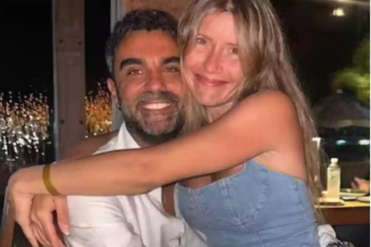 Una pareja sonriente se abraza en un ambiente nocturno con luces de fondo. Una pareja sonriente se abraza en un ambiente nocturno con luces de fondo.