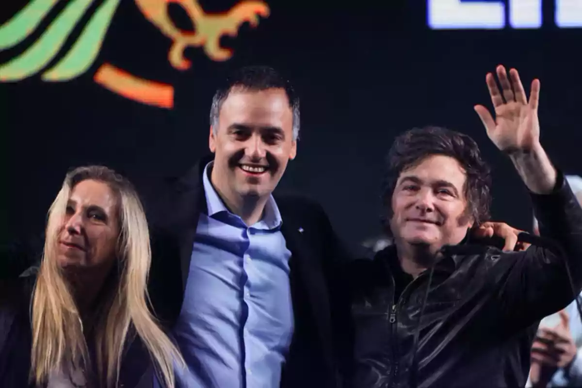 Three people smile and wave at a public event. Three people smile and wave at a public event.