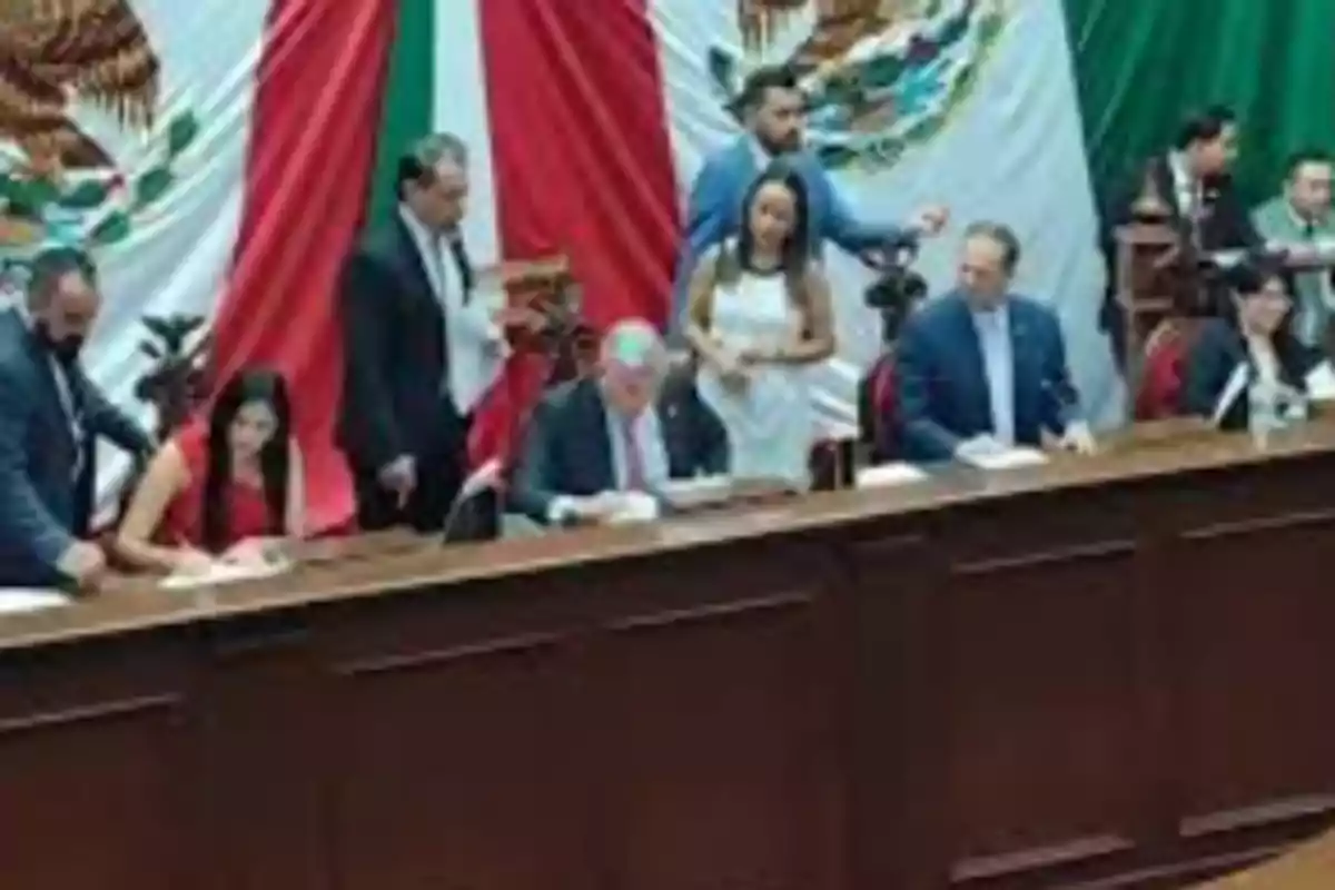 Un grupo de personas en una sala de reuniones con una bandera de México de fondo. Un grupo de personas en una sala de reuniones con una bandera de México de fondo.