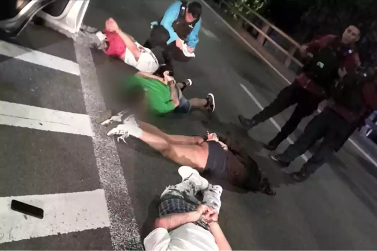 People detained on the ground with their hands tied while police officers watch on a street.