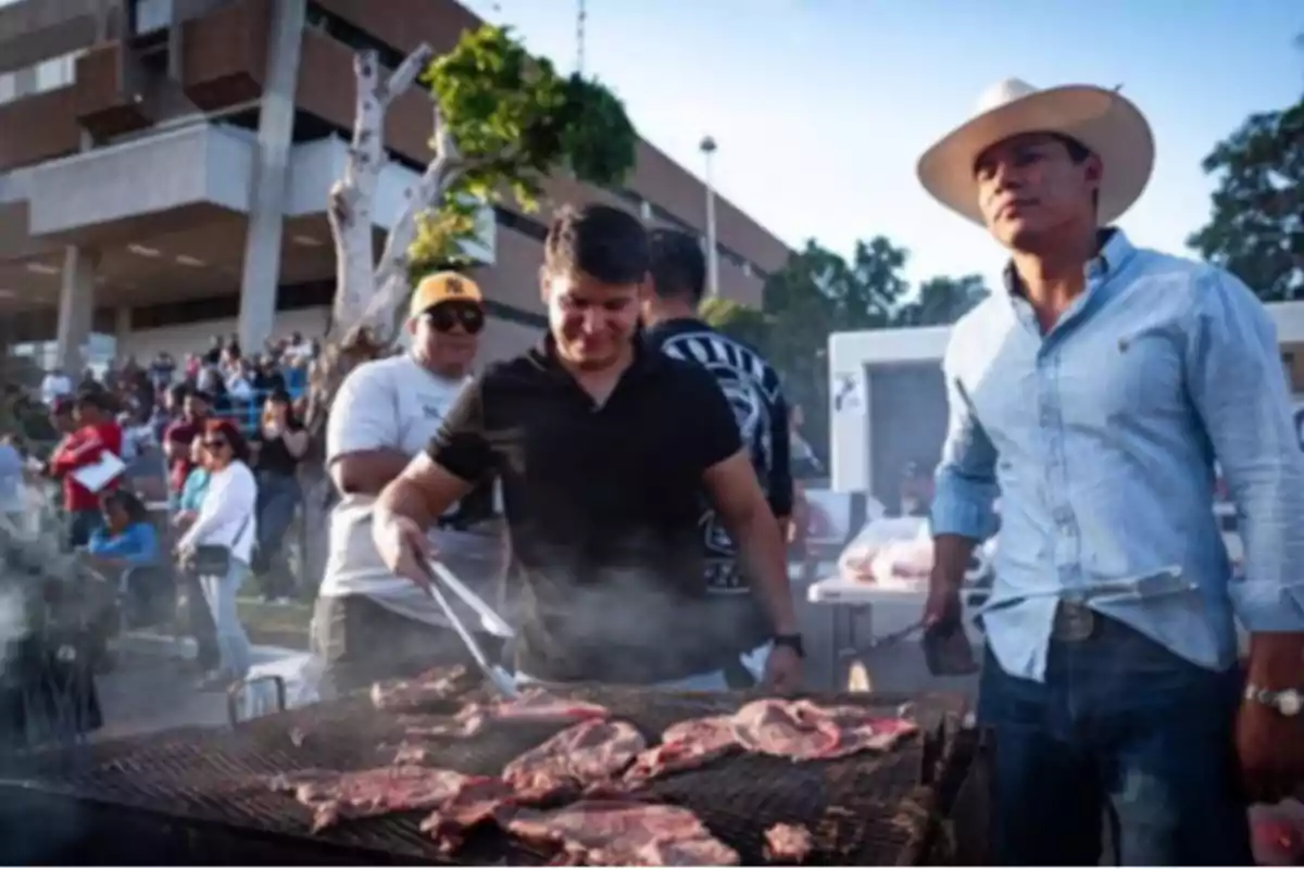Un grupo de personas asando carne en una parrilla al aire libre durante un evento concurrido.