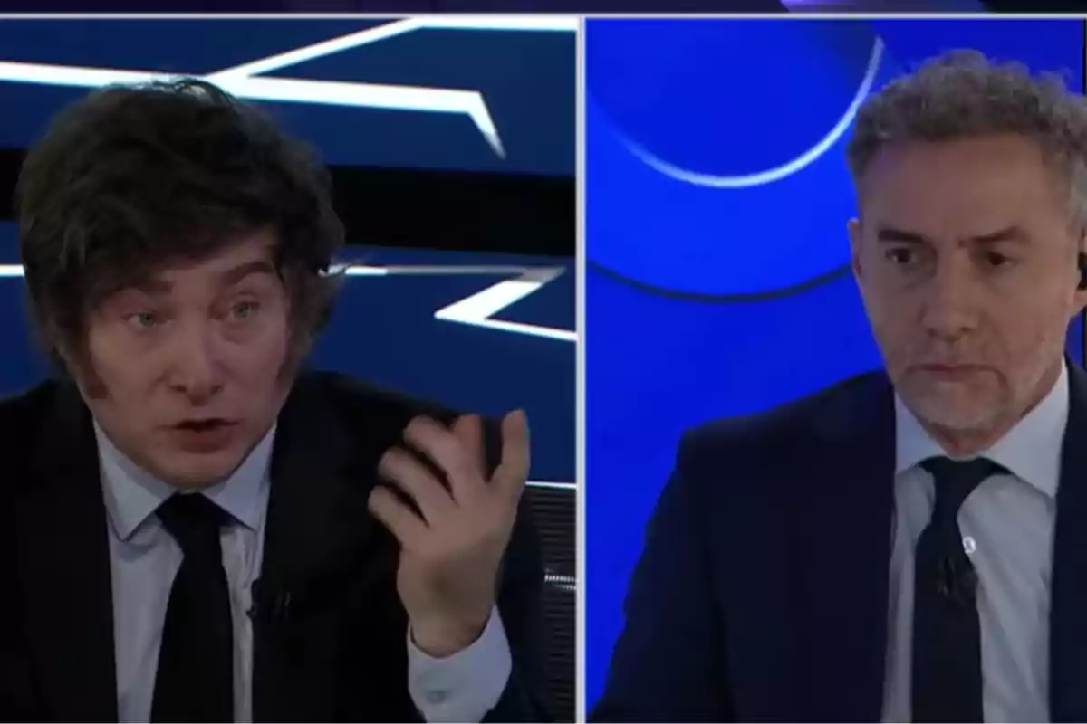 Two men on a television show, one gesturing while speaking and the other listening alertly.