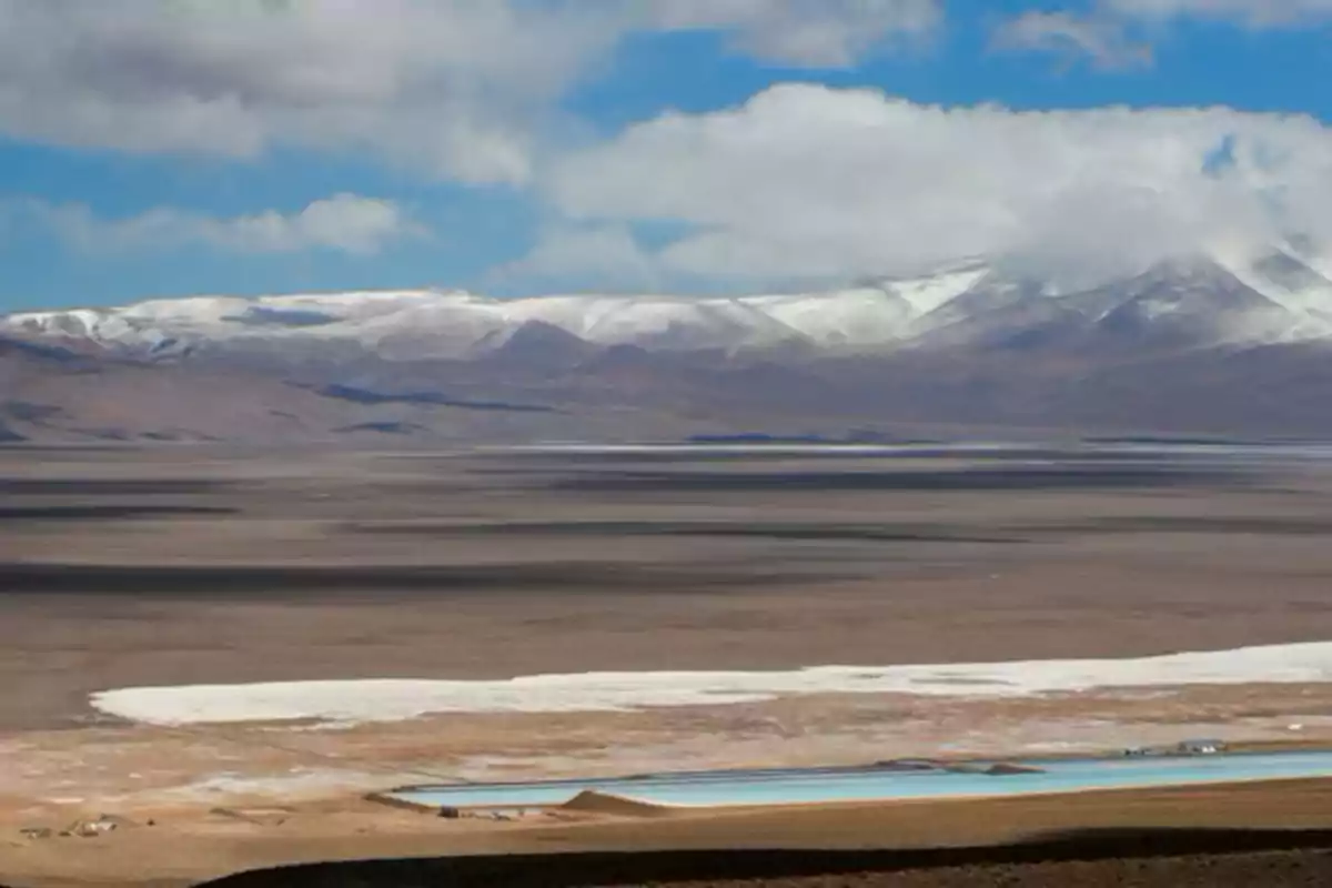 Paisaje desértico con montañas nevadas al fondo y un cielo parcialmente nublado. Paisaje desértico con montañas nevadas al fondo y un cielo parcialmente nublado.