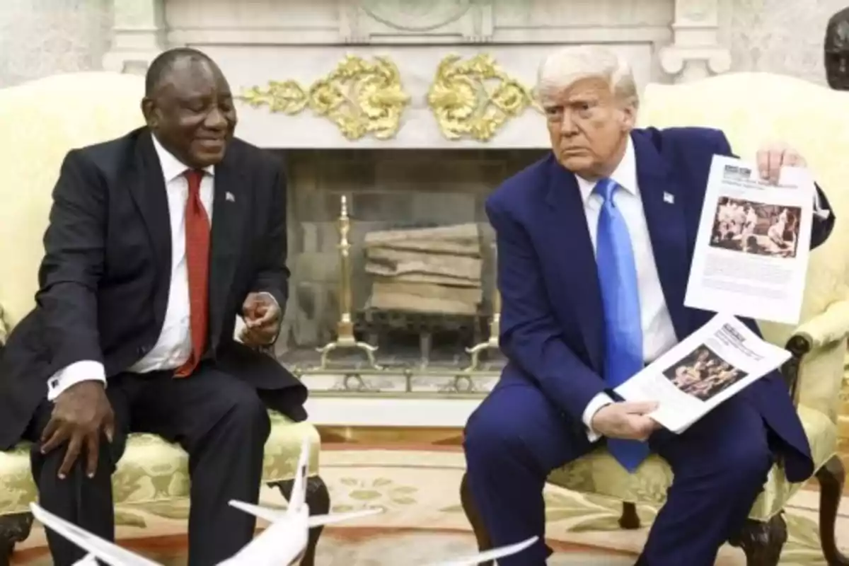 Two men sitting in an elegant room, one of them holding documents while the other smiles.