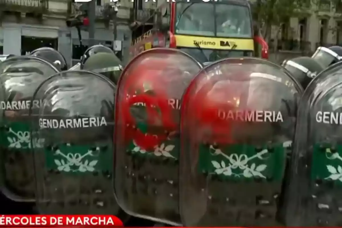 Un grupo de escudos de la gendarmería alineados frente a un autobús turístico en una calle urbana.
