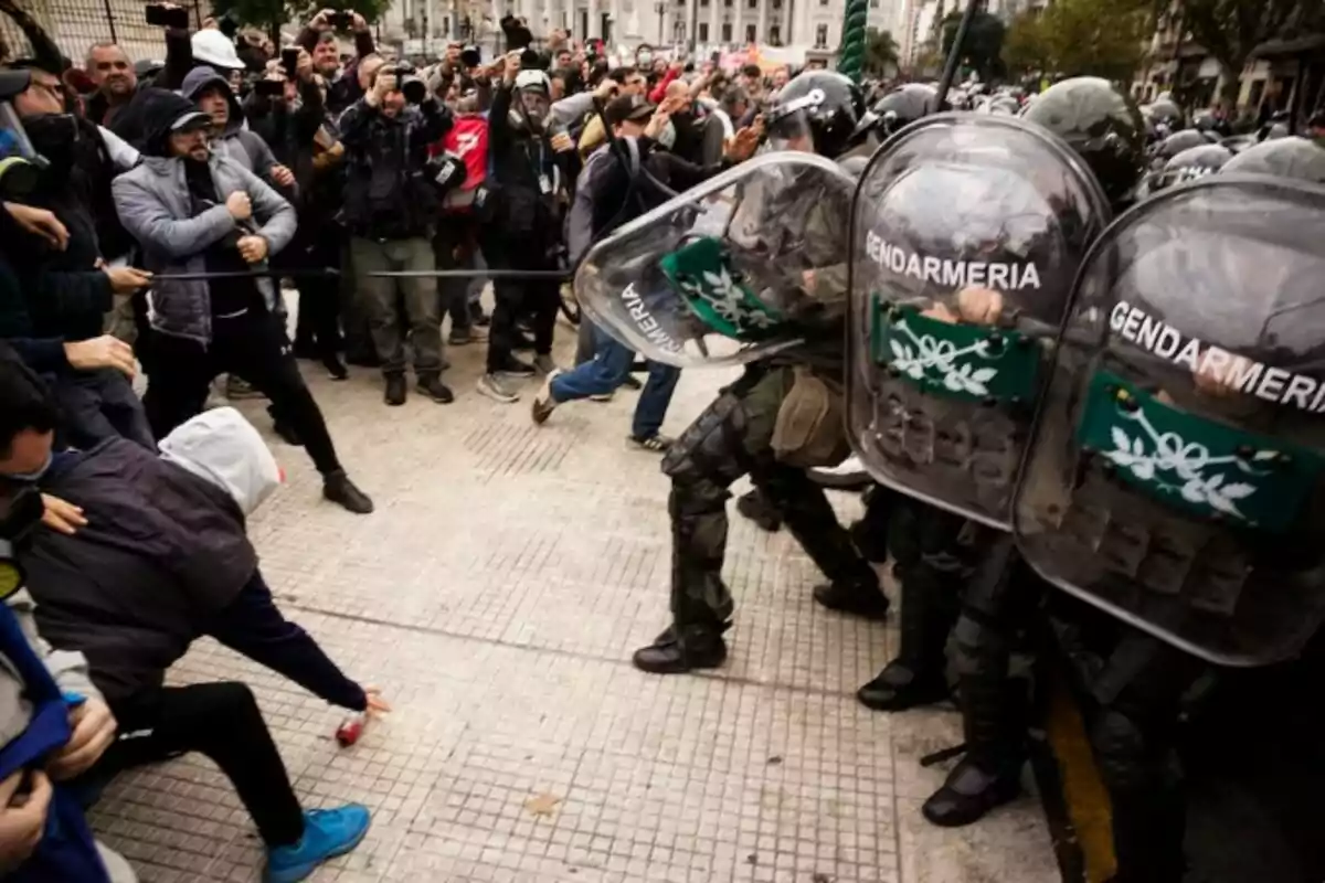 Un grupo de manifestantes se enfrenta a un cordón de gendarmes con escudos en una protesta en la calle. Un grupo de manifestantes se enfrenta a un cordón de gendarmes con escudos en una protesta en la calle.