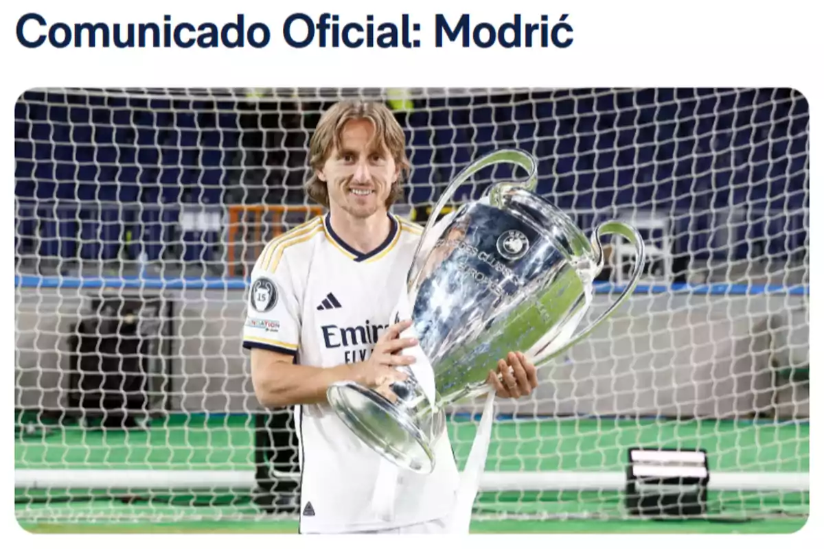 A player in a white uniform holds a large silver trophy in front of a goal. A player in a white uniform holds a large silver trophy in front of a goal.