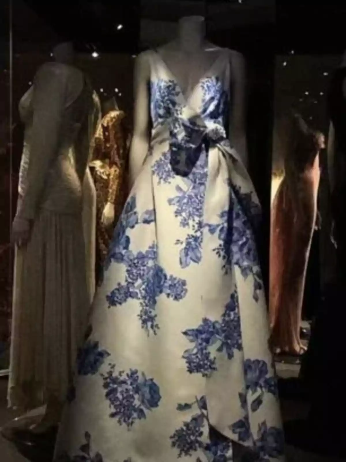 Un vestido de noche blanco con estampado floral azul exhibido en un maniquí en un entorno de museo o galería. Un vestido de noche blanco con estampado floral azul exhibido en un maniquí en un entorno de museo o galería.