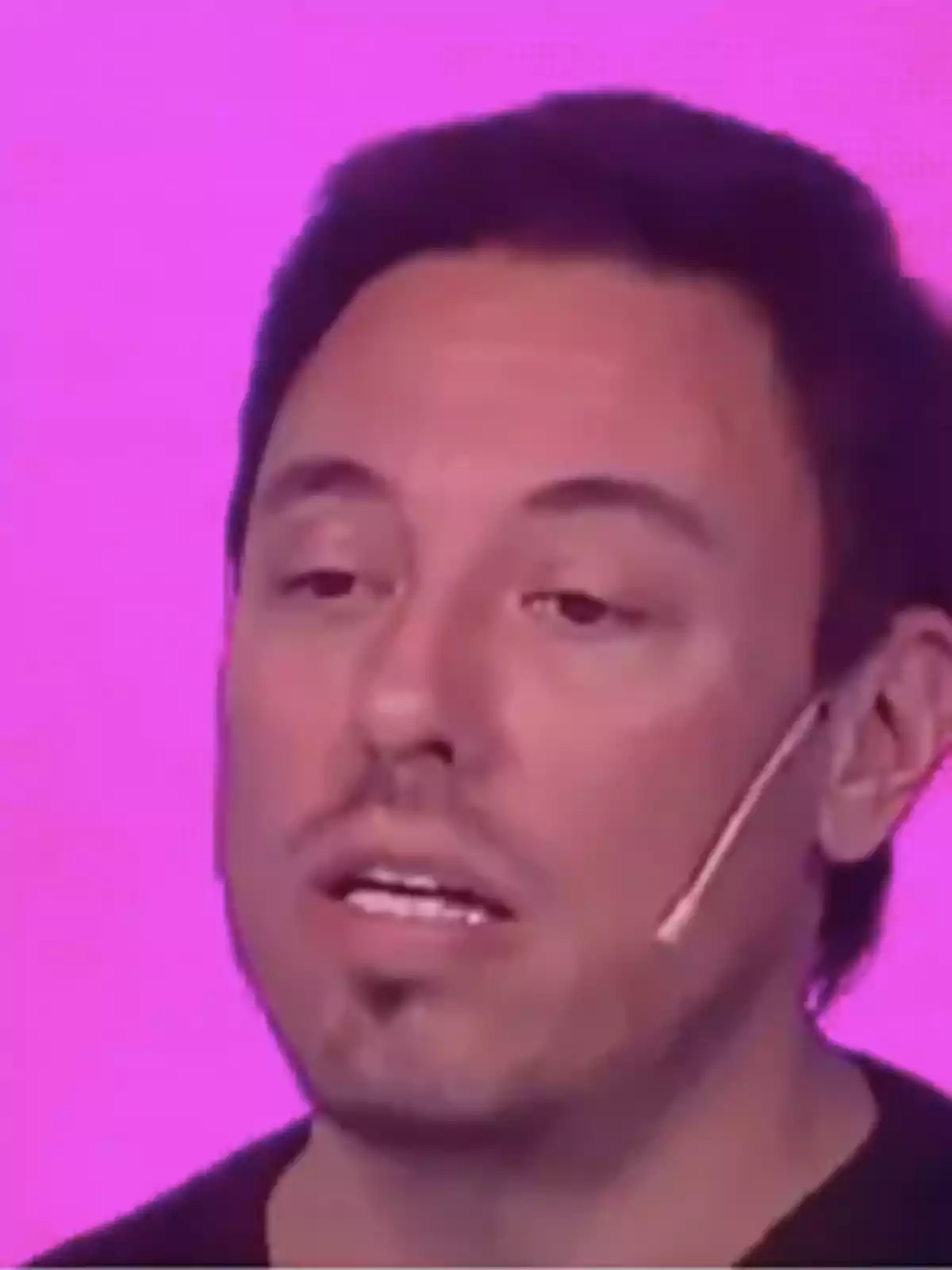 A man with a headset microphone against a pink background. A man with a headset microphone against a pink background.
