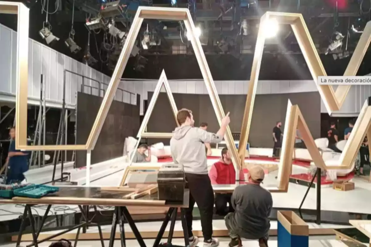 Several people are working on installing large golden letters on a modern television set. Several people are working on installing large golden letters on a modern television set.