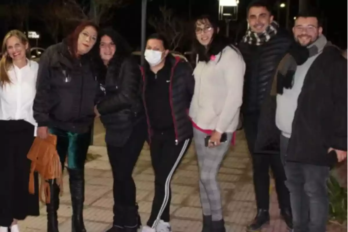 A group of people smiles and poses together outdoors at night, some wearing warm clothes and scarves. A group of people smiles and poses together outdoors at night, some wearing warm clothes and scarves.