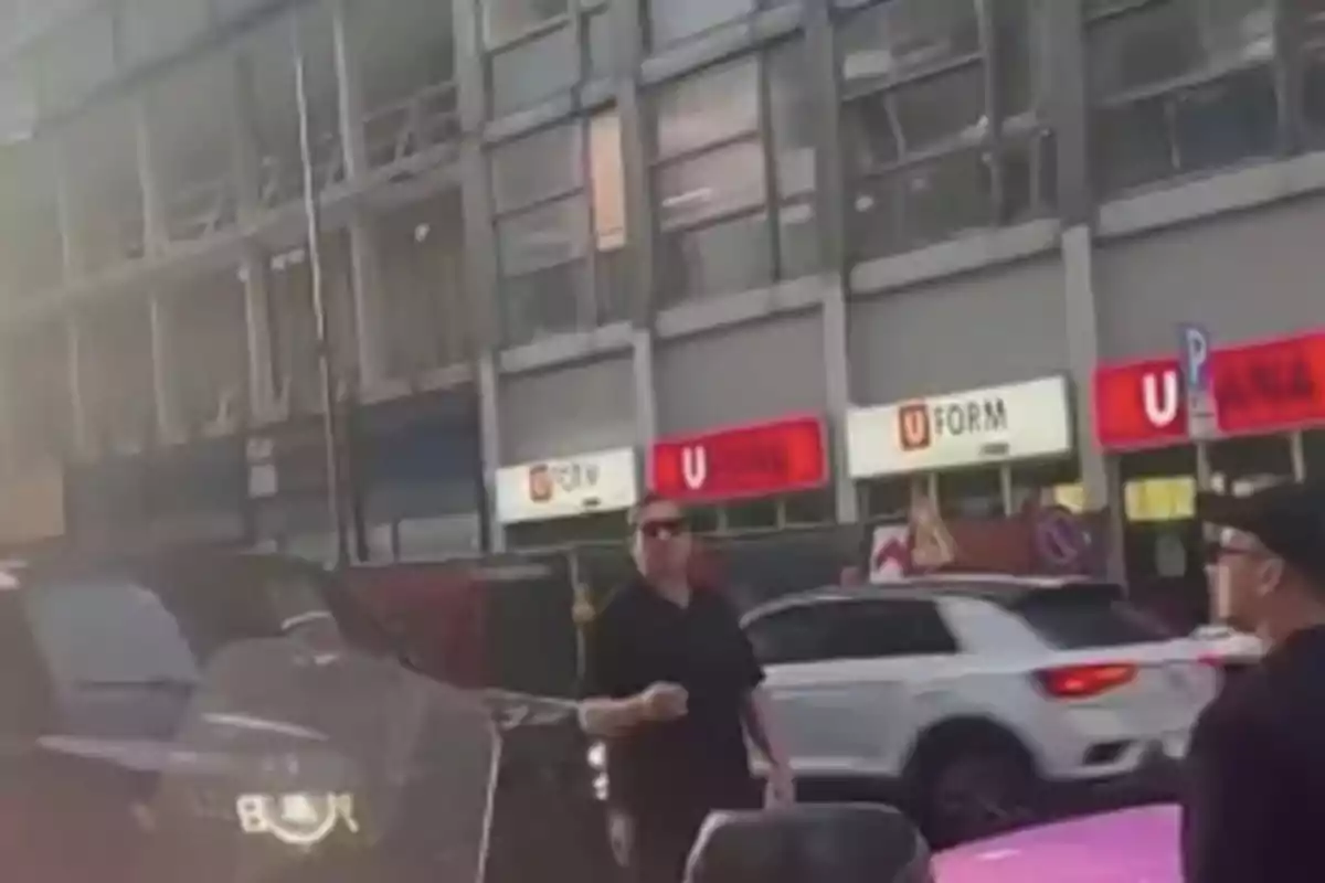 Dos hombres de pie en una calle concurrida con varios autos y un edificio de fondo que tiene letreros luminosos Dos hombres de pie en una calle concurrida con varios autos y un edificio de fondo que tiene letreros luminosos