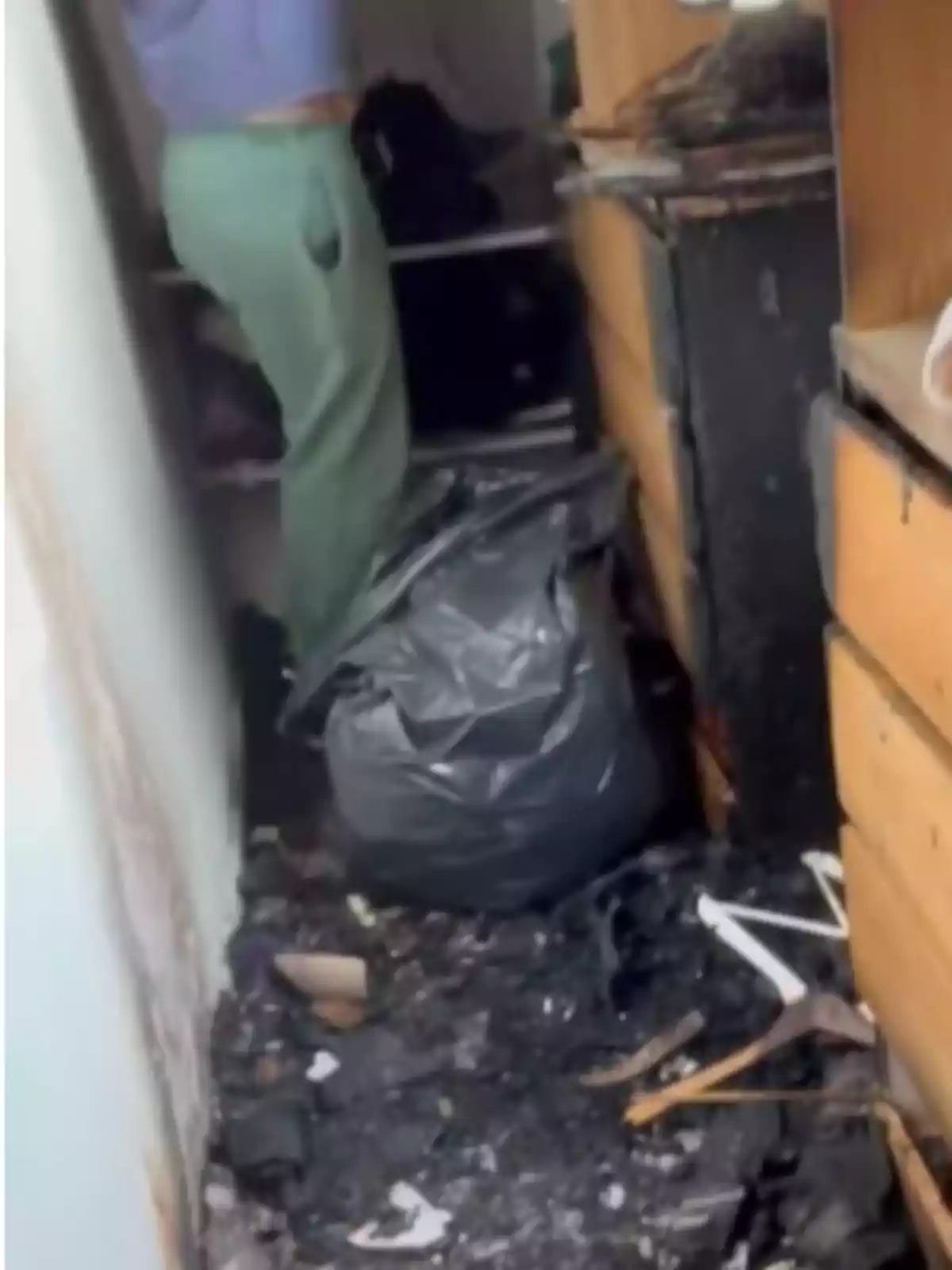Persona de pie en una habitación con muebles quemados, suelo cubierto de cenizas y una bolsa de basura negra Persona de pie en una habitación con muebles quemados, suelo cubierto de cenizas y una bolsa de basura negra