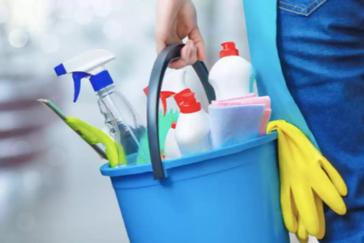 Person holding a blue bucket with cleaning products, yellow gloves, and cloths