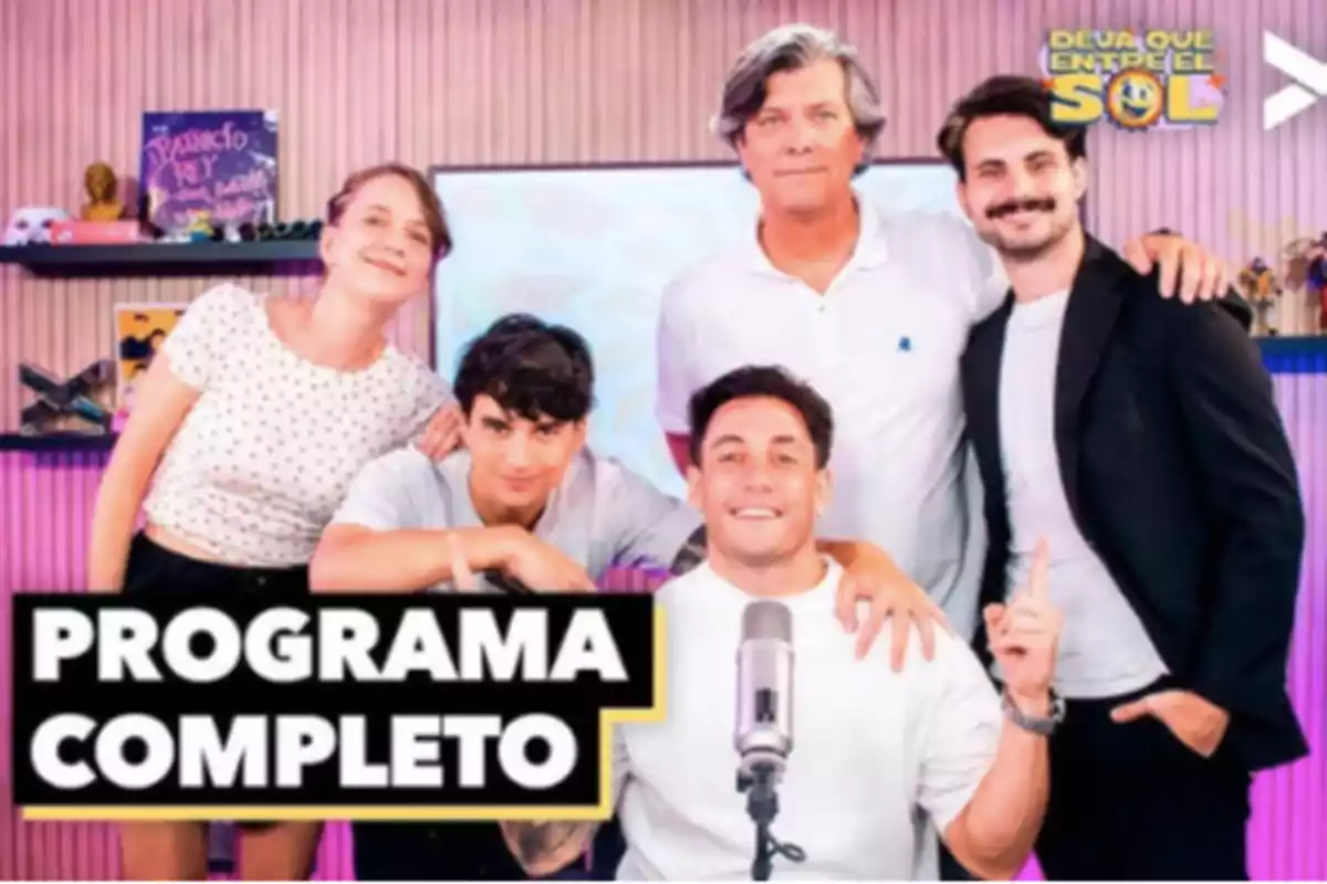 Cinco personas posan sonrientes en un estudio de grabación con un micrófono al frente y un letrero que dice programa completo Cinco personas posan sonrientes en un estudio de grabación con un micrófono al frente y un letrero que dice programa completo