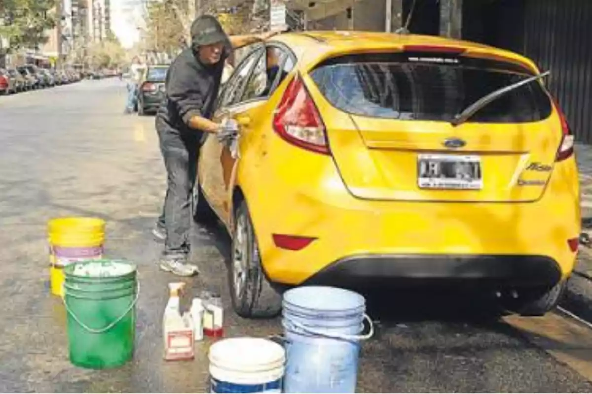 Man washing a yellow car on the street with several buckets and cleaning products around. Man washing a yellow car on the street with several buckets and cleaning products around.