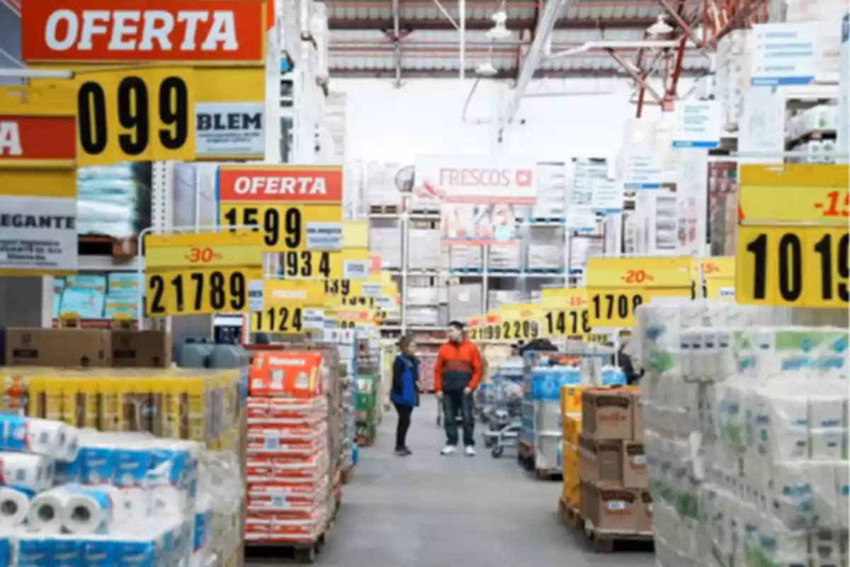 Wholesale supermarket aisle with sale signs and stacked products, two people talking in the center