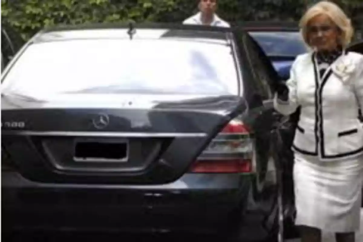 Blonde woman dressed in white with black details getting out of a black Mercedes-Benz car Blonde woman dressed in white with black details getting out of a black Mercedes-Benz car