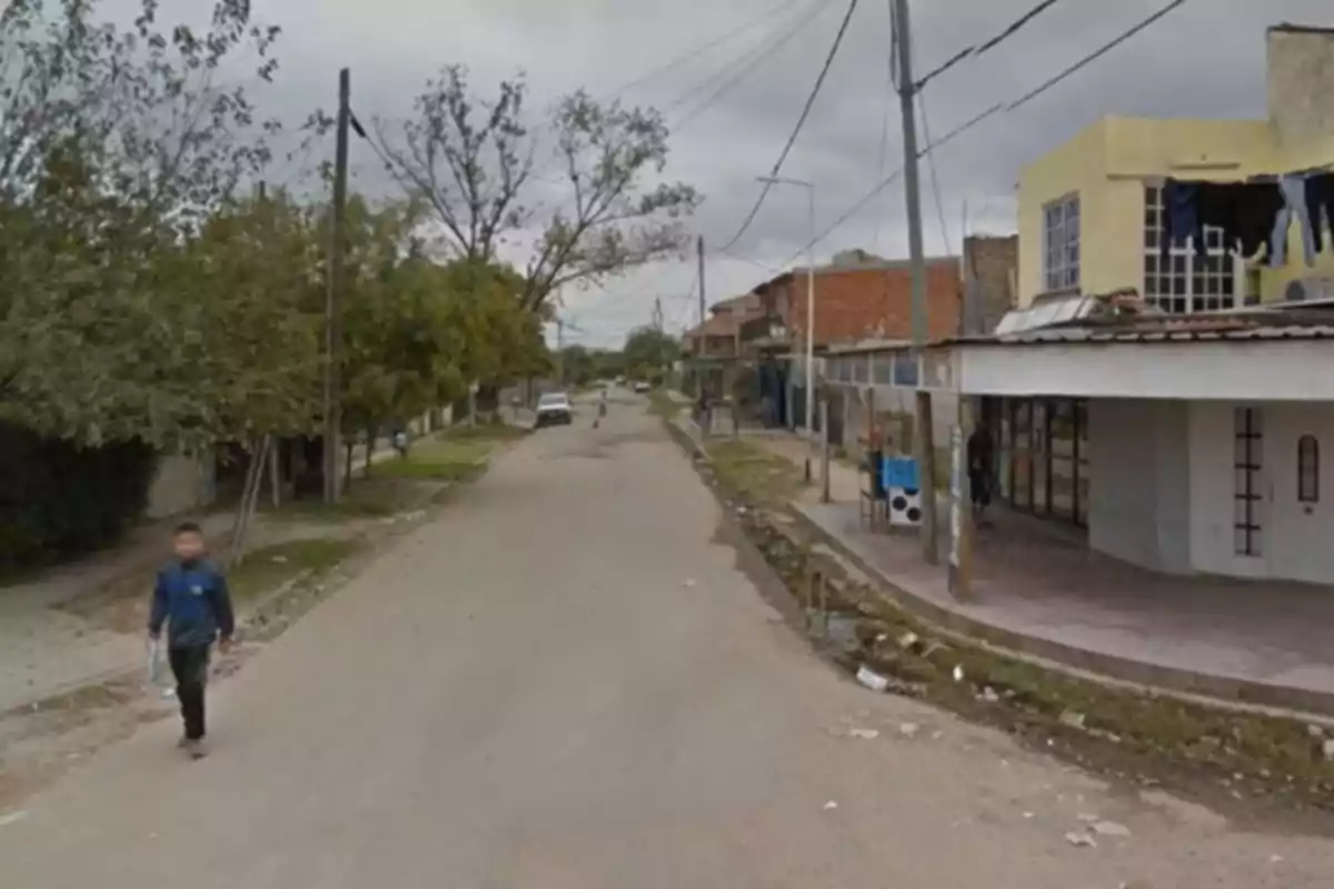 Neighborhood street with houses on the sides, trees, power lines, and a person walking on the sidewalk under a cloudy sky Neighborhood street with houses on the sides, trees, power lines, and a person walking on the sidewalk under a cloudy sky