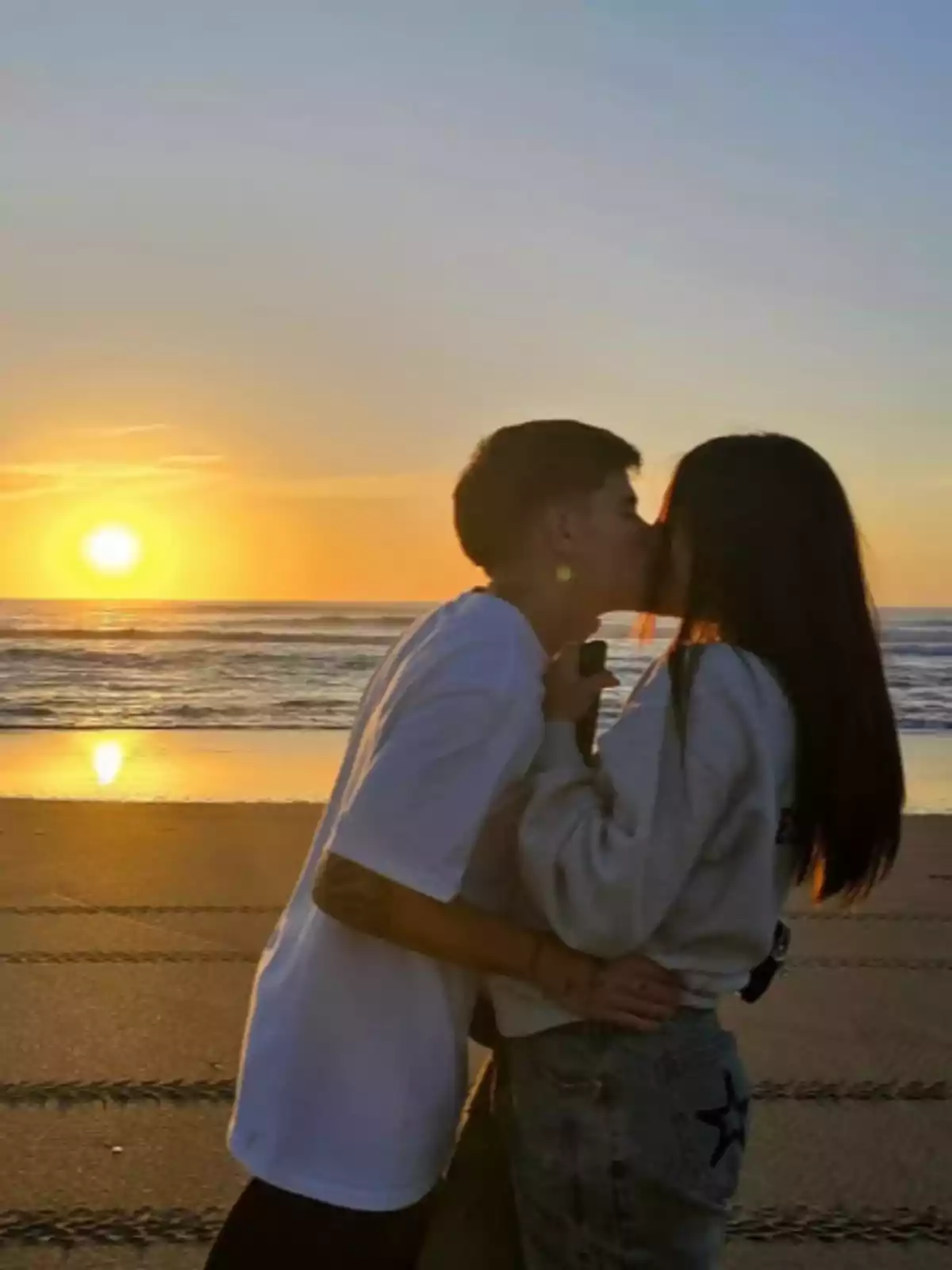 Couple kissing on the beach at sunset with the sun reflecting on the sea Couple kissing on the beach at sunset with the sun reflecting on the sea