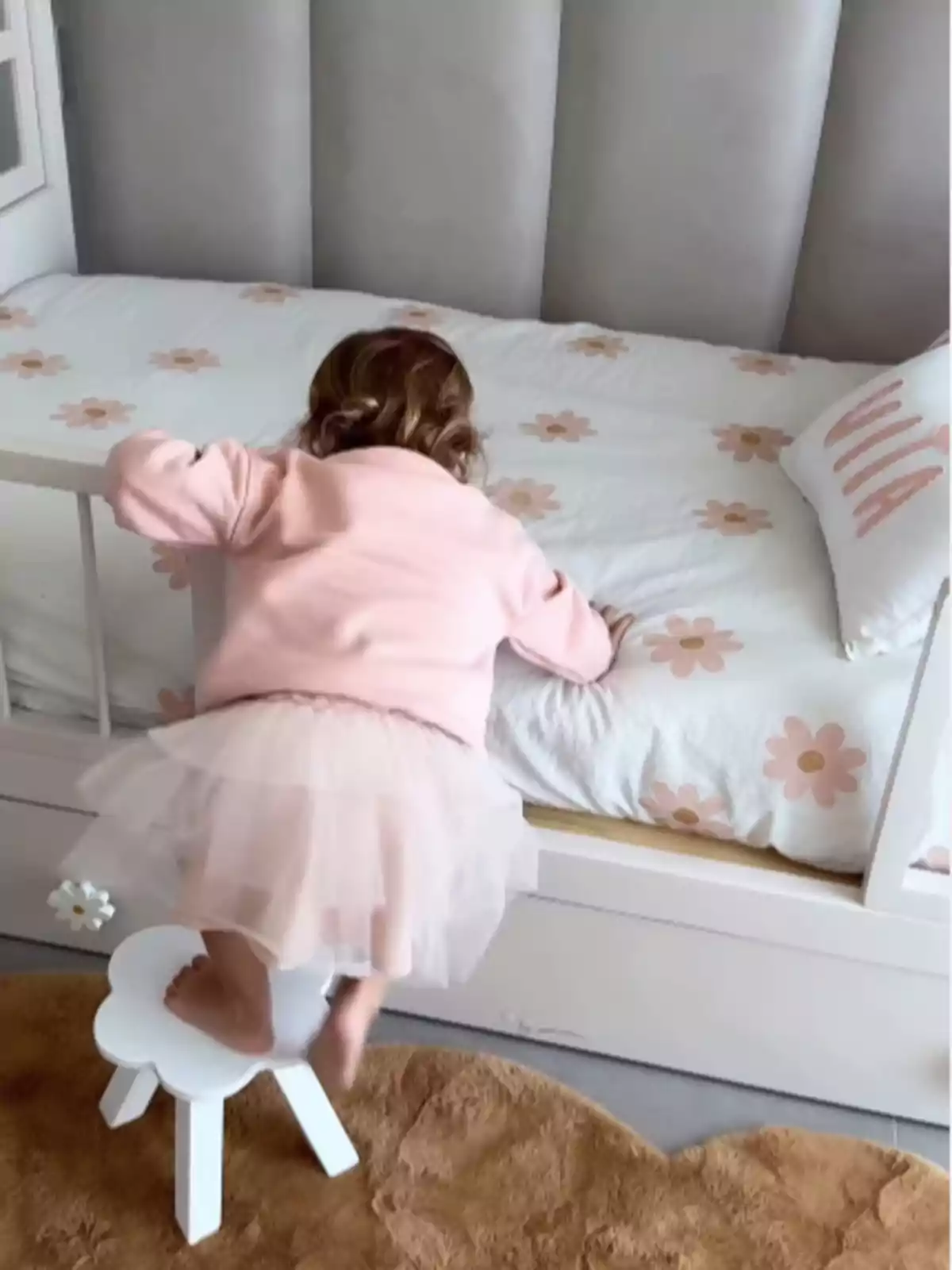 Niña pequeña subiendo a una cama usando un banquito blanco en una habitación infantil decorada en tonos suaves Niña pequeña subiendo a una cama usando un banquito blanco en una habitación infantil decorada en tonos suaves