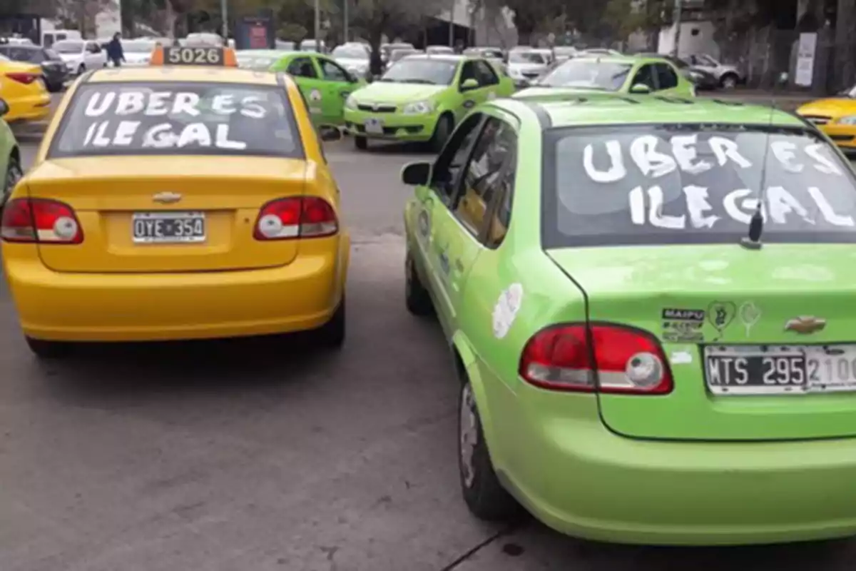 Yellow and green taxis with messages in the rear windows saying Uber is illegal parked on the street