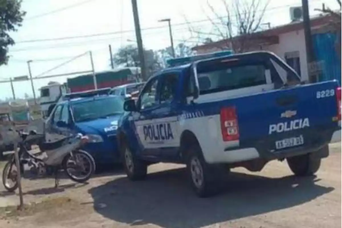 Two police patrol cars and a motorcycle parked on a dirt street in a residential neighborhood during the day