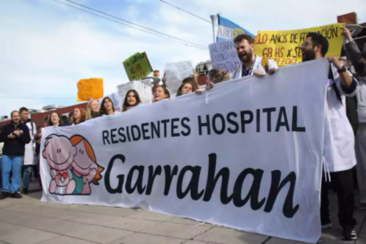 A group of people in lab coats holding a large white banner that reads "Hospital Garrahan Residents" during an outdoor demonstration