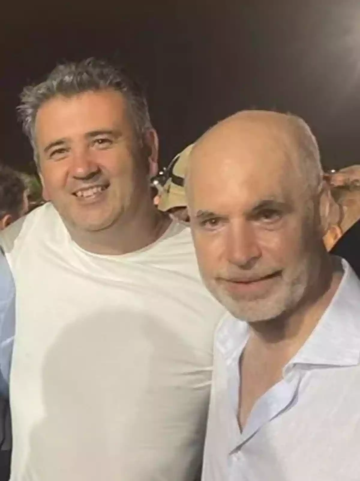 Two men pose together and smile in a photo taken at night.
