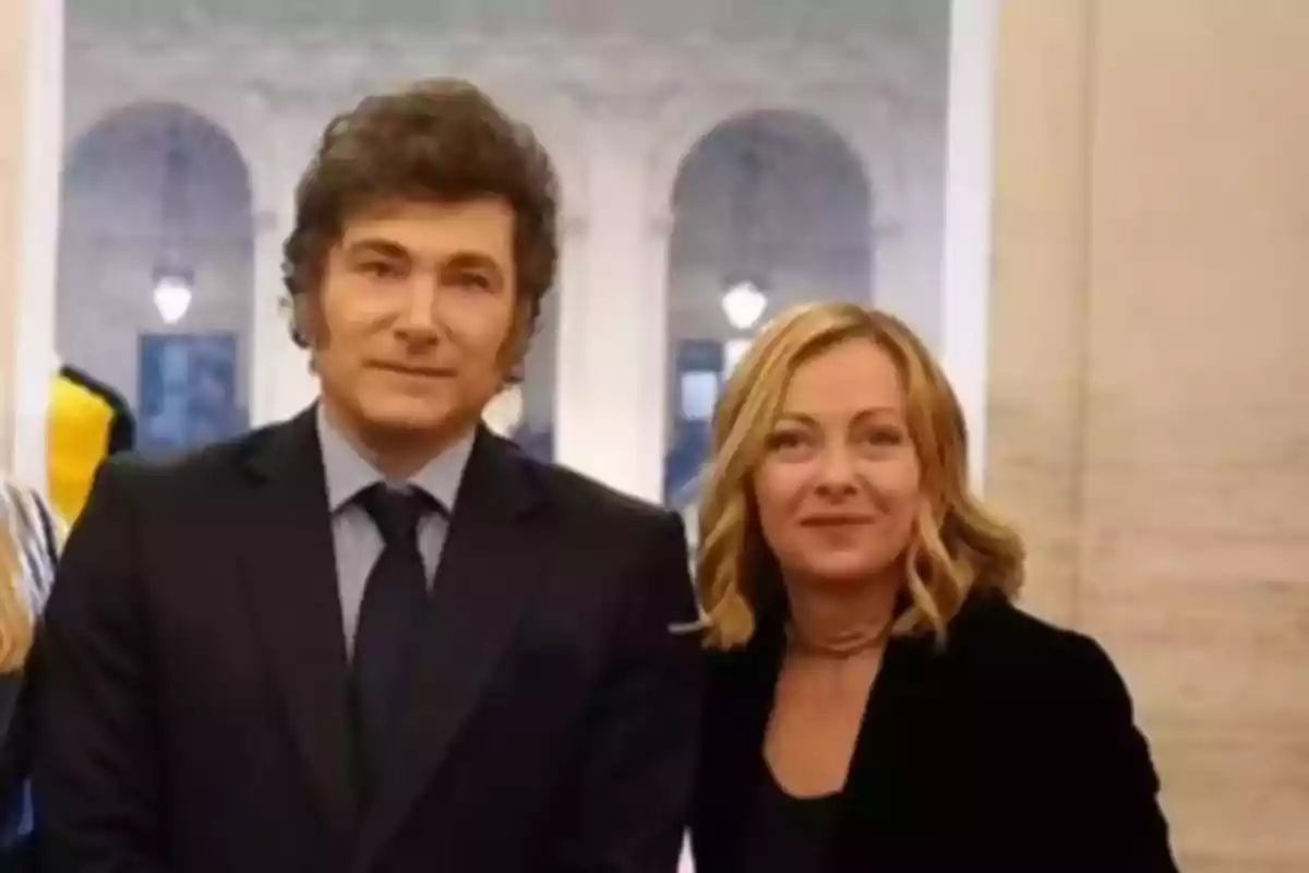 Dos personas posan juntas en un entorno elegante con columnas y luces al fondo Dos personas posan juntas en un entorno elegante con columnas y luces al fondo