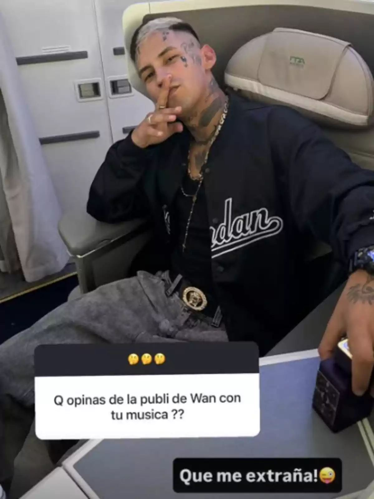 Un joven con tatuajes en la cara y el cuello está sentado en un asiento de avión de clase ejecutiva, viste una chaqueta negra y pantalones grises, sostiene un cigarro y una caja, y en la imagen aparecen preguntas y respuestas sobre su música y publicidad. Un joven con tatuajes en la cara y el cuello está sentado en un asiento de avión de clase ejecutiva, viste una chaqueta negra y pantalones grises, sostiene un cigarro y una caja, y en la imagen aparecen preguntas y respuestas sobre su música y publicidad.