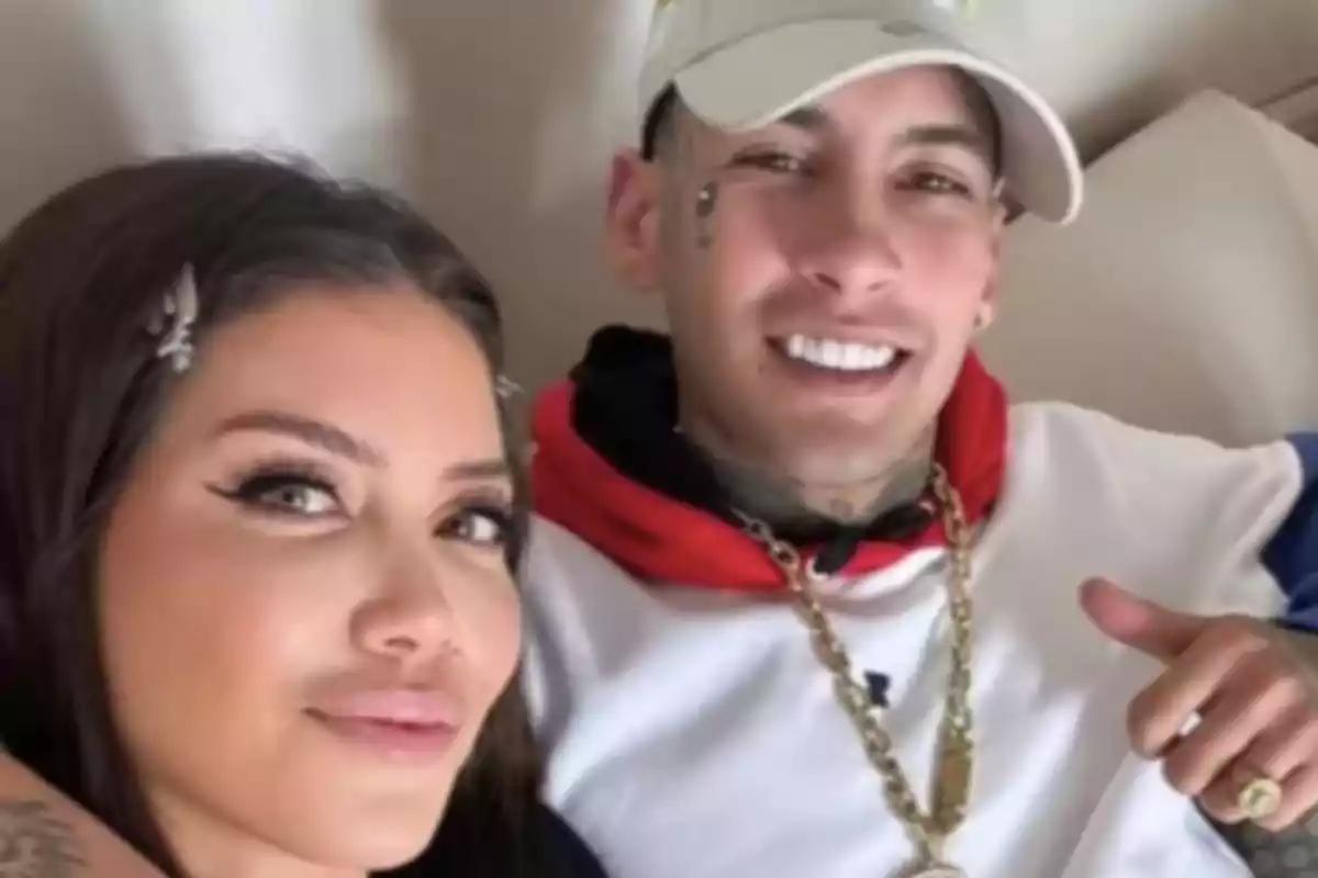 A woman and a man smile together as they pose for a selfie indoors.