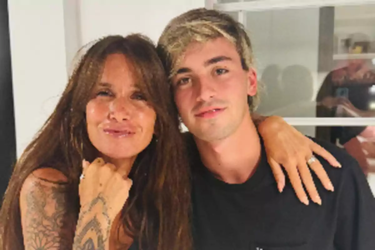 A woman with long hair and tattoos on her arm hugs a blond young man as they both smile at the camera. A woman with long hair and tattoos on her arm hugs a blond young man as they both smile at the camera.