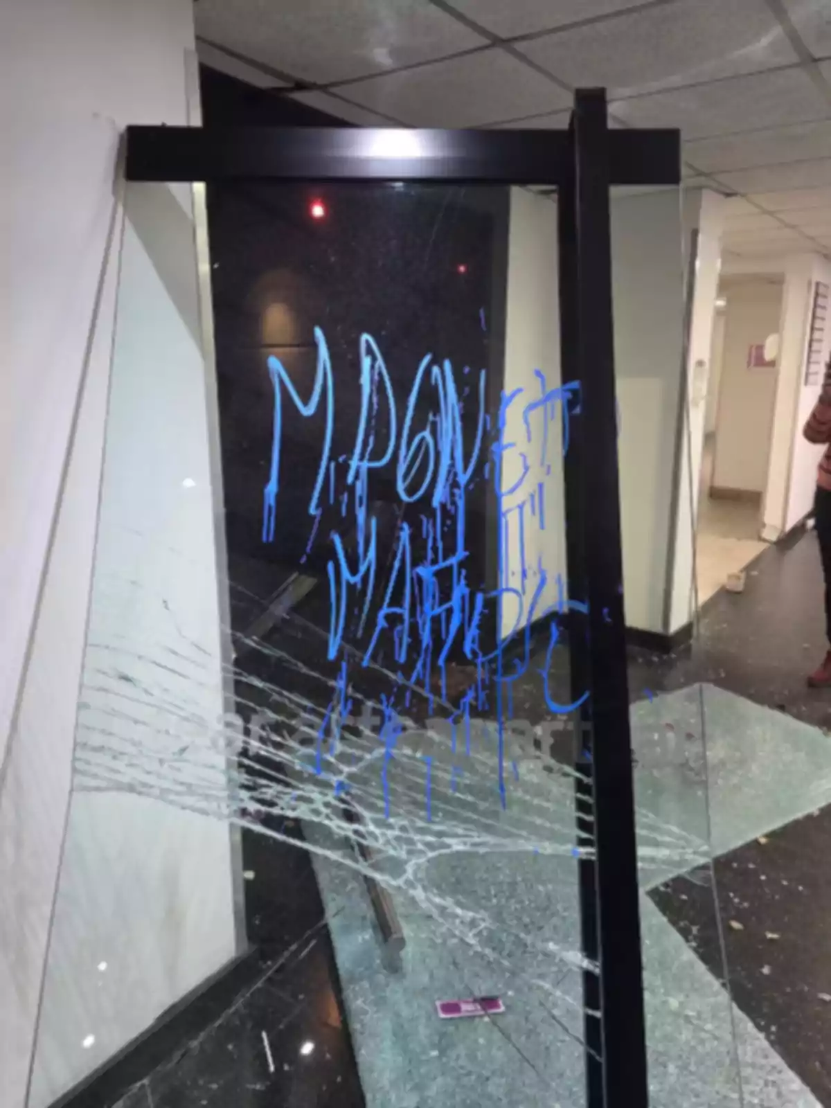 Puerta de vidrio rota con grafiti azul y fragmentos de vidrio en el suelo Puerta de vidrio rota con grafiti azul y fragmentos de vidrio en el suelo