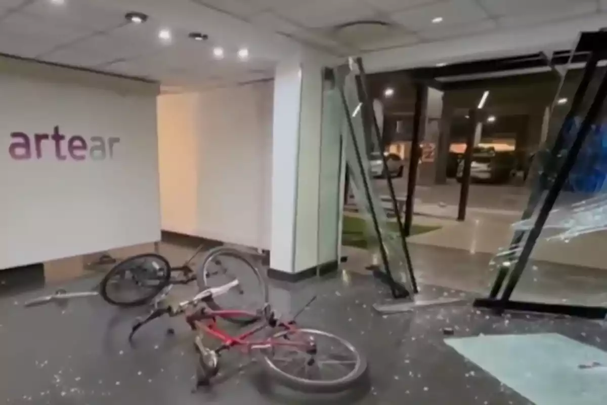 Oficina con el logo de Artear en la pared, una bicicleta tirada en el suelo y una puerta de vidrio rota con fragmentos esparcidos