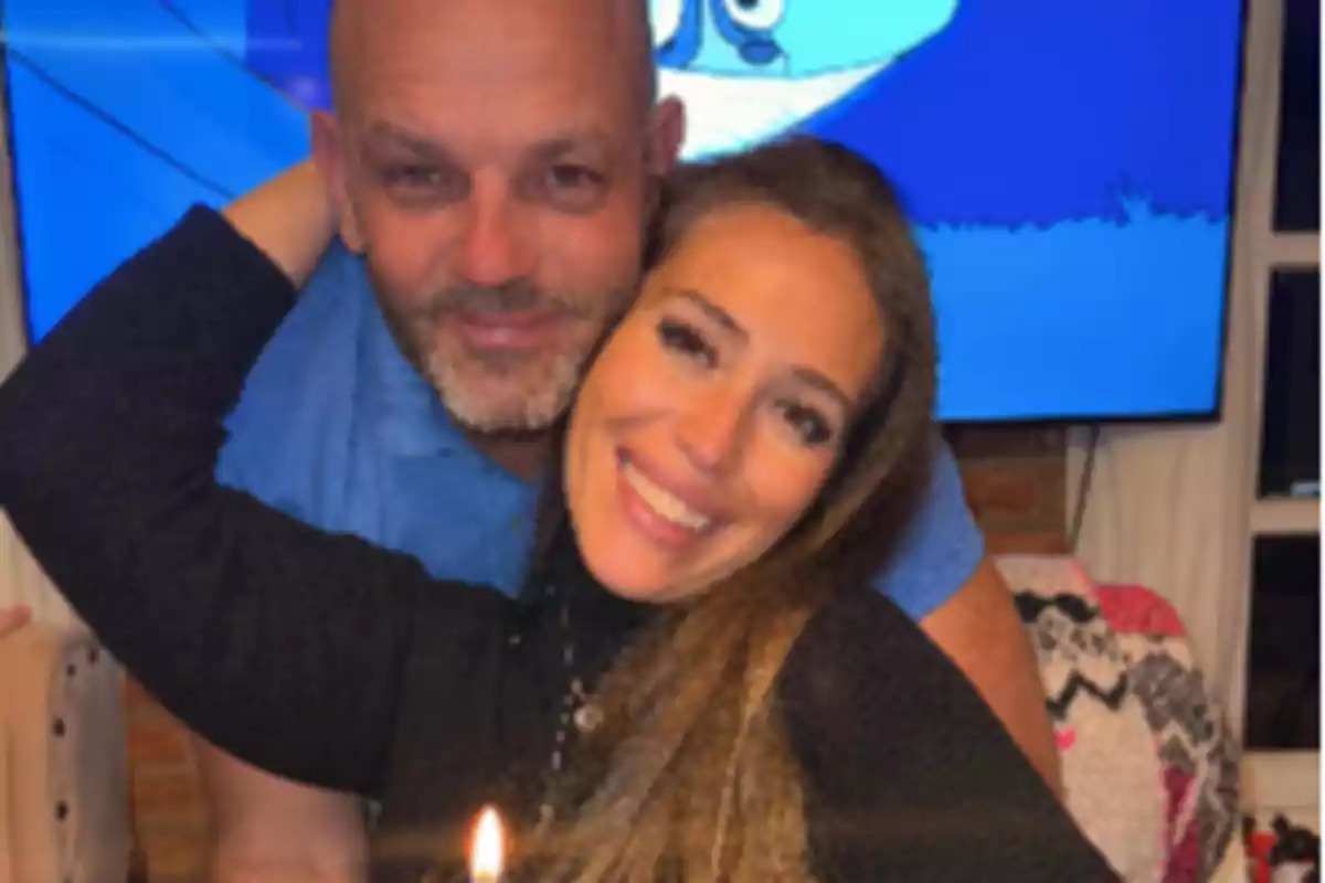 Pareja abrazada sonriendo frente a una vela encendida con una pantalla azul de fondo Pareja abrazada sonriendo frente a una vela encendida con una pantalla azul de fondo