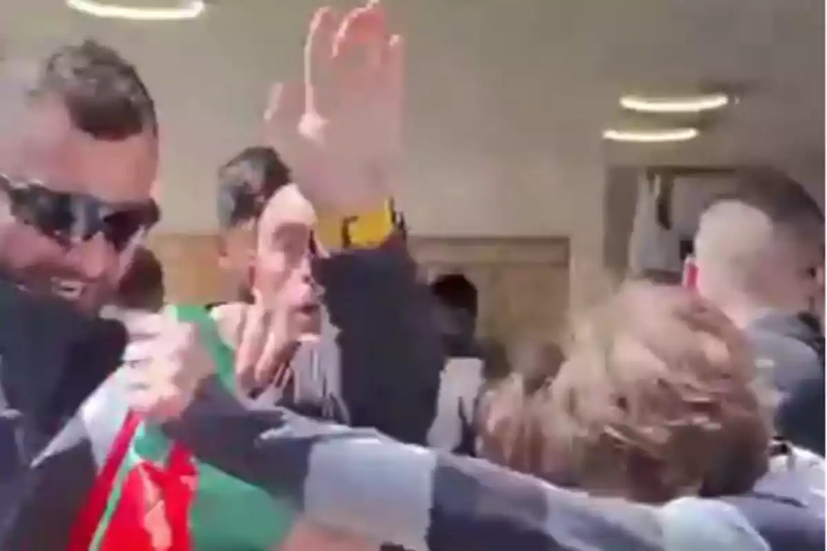 Varias personas se encuentran reunidas en un espacio cerrado, algunas levantan los brazos y una de ellas lleva gafas oscuras.