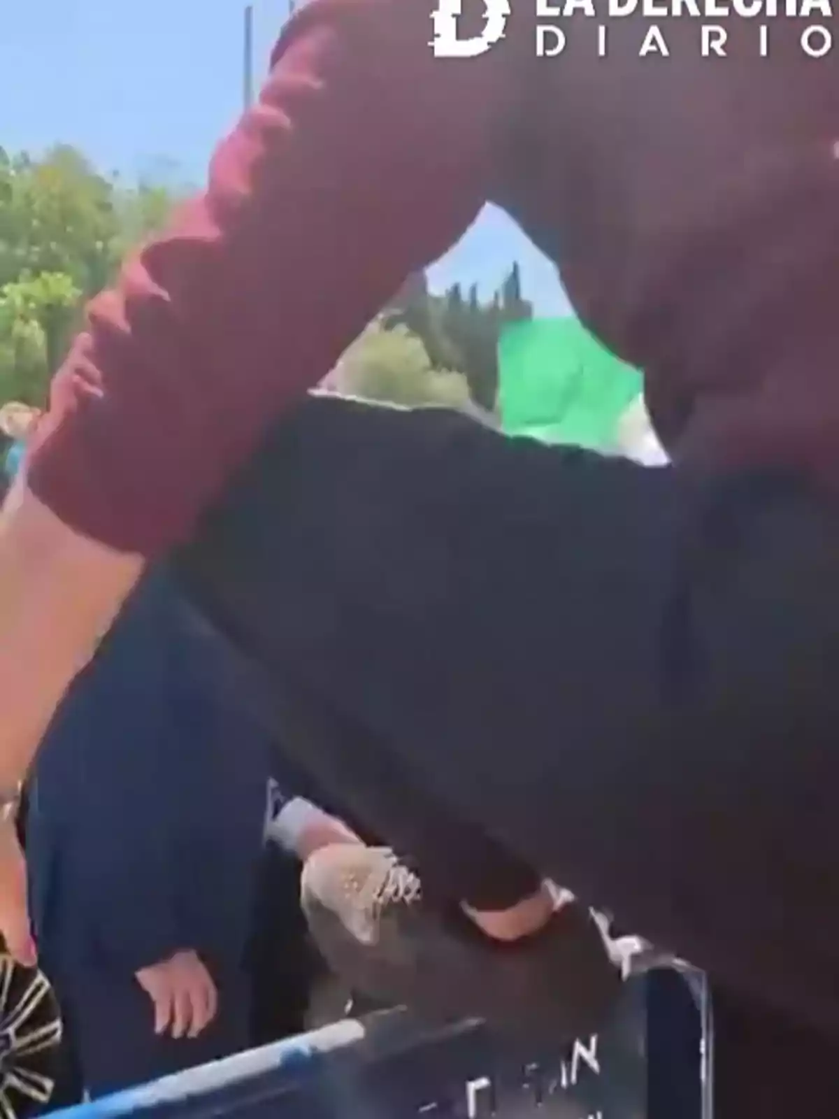 Persona saltando una valla metálica durante el día en un espacio al aire libre con otras personas alrededor Persona saltando una valla metálica durante el día en un espacio al aire libre con otras personas alrededor