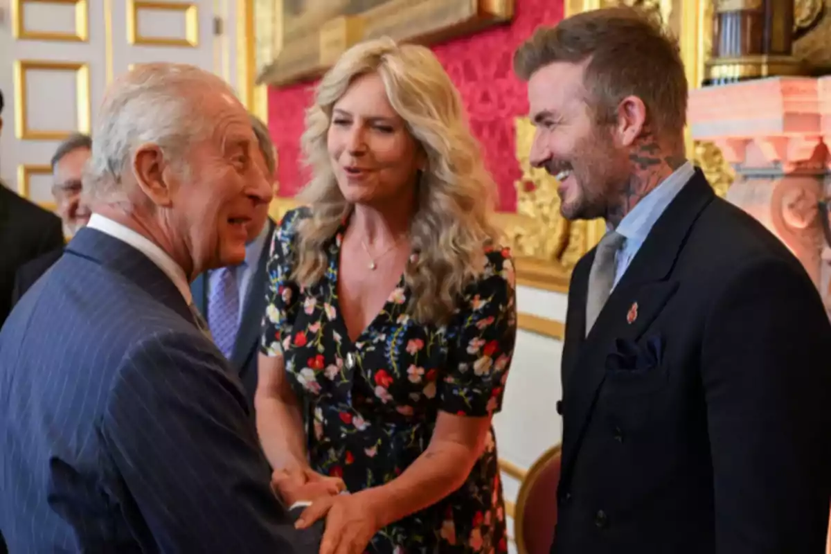 Three elegantly dressed people are conversing and smiling in a room decorated with golden details and red walls. Three elegantly dressed people are conversing and smiling in a room decorated with golden details and red walls.