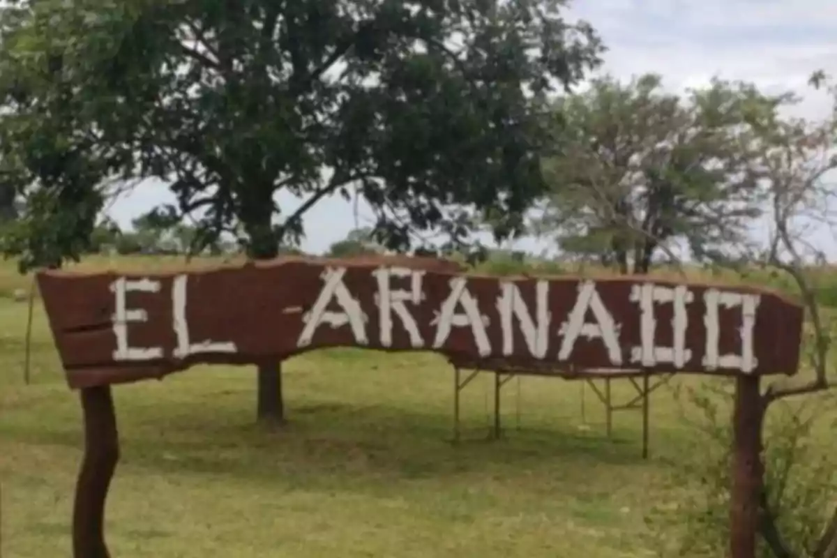 Wooden sign with the text EL ARANAO in a natural setting with trees and grass.