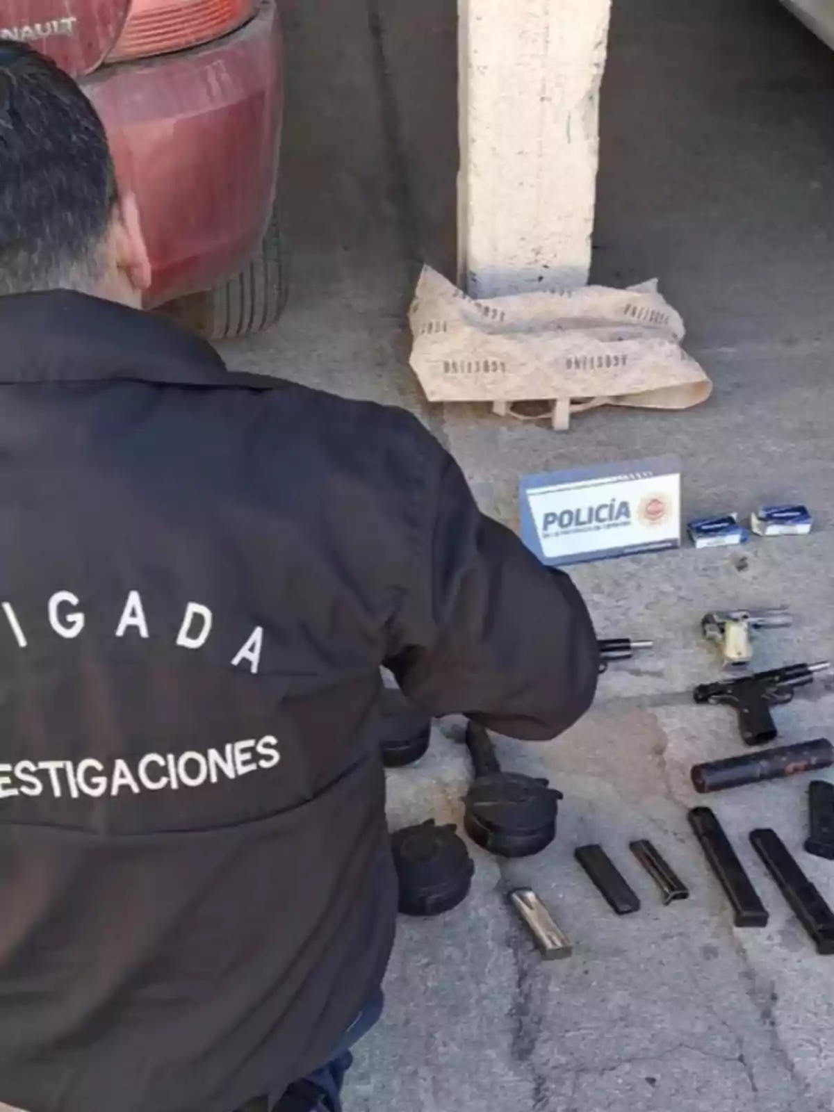 Investigative police officer inspecting several seized firearms, magazines, and ammunition next to a red car Investigative police officer inspecting several seized firearms, magazines, and ammunition next to a red car